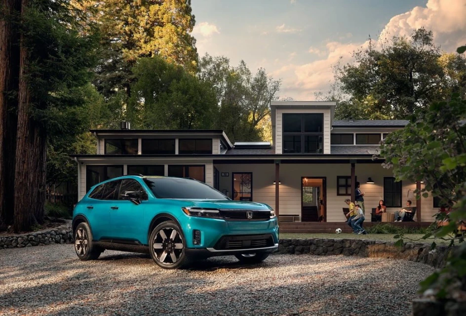 A light-blue Honda Prologue electric SUV is parked in front of a modern two-story home with children and adults on the porch.