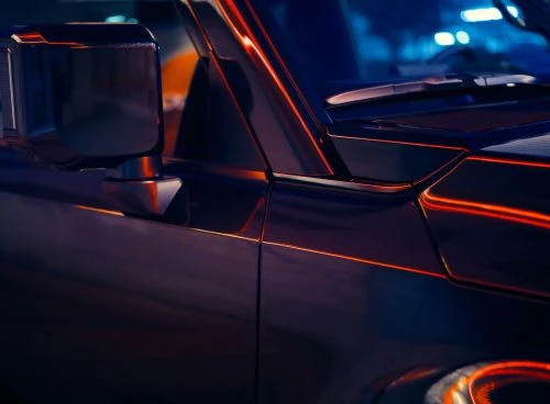 Close-up of a dark SUV with orange reflective lines, showcasing its side mirror, front door, and part of the hood under blue ambient light.