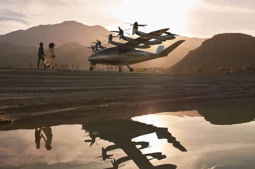 Aerial vehicle sits on runway with a couple walking in the sunset reflecting in the water. Mountains are in the background.