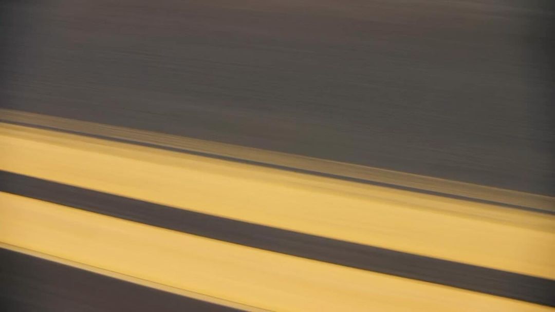 Abstract blurred view of black asphalt road surface with yellow painted lane markings, creating a sense of speed and motion.