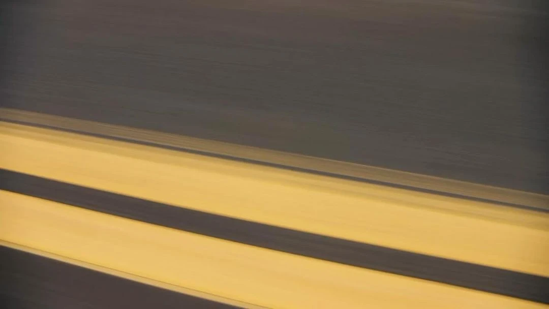 Abstract blurred view of black asphalt road surface with yellow painted lane markings, creating a sense of speed and motion.