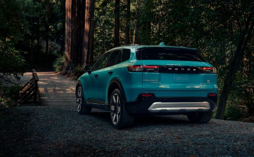 Teal Henge SUV parked on a gravel path, surrounded by tall trees in a forest setting. Outdoor scene captures automotive design.