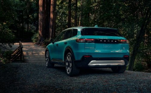 Teal Henge SUV parked on a gravel path, surrounded by tall trees in a forest setting. Outdoor scene captures automotive design.