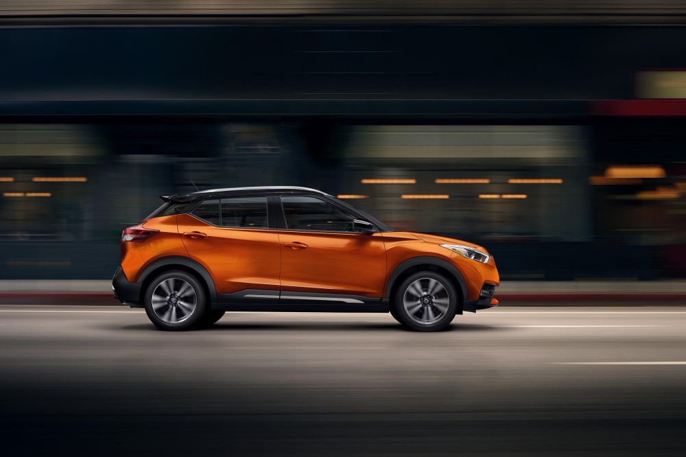 Orange crossover SUV driving on a road with blurred motion in the background, showcasing its design and urban environment.
