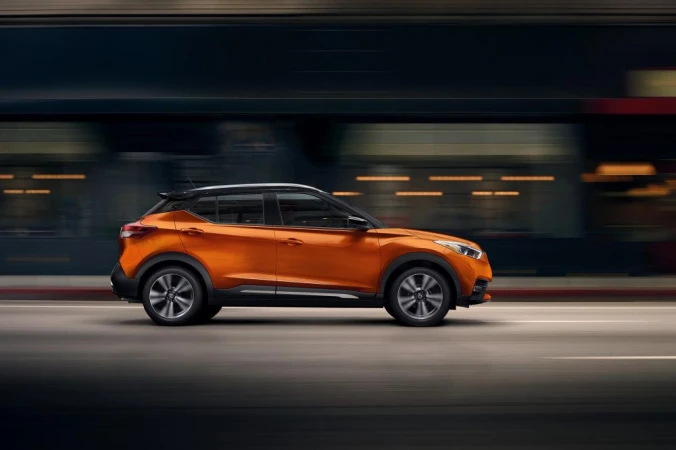 Orange crossover SUV driving on a road with blurred motion in the background, showcasing its design and urban environment.