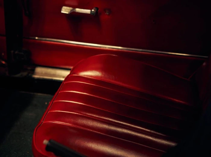 Close-up interior view of a classic car with glossy red leather bucket seats and a matching red door panel.