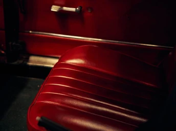 Close-up interior view of a classic car with glossy red leather bucket seats and a matching red door panel.