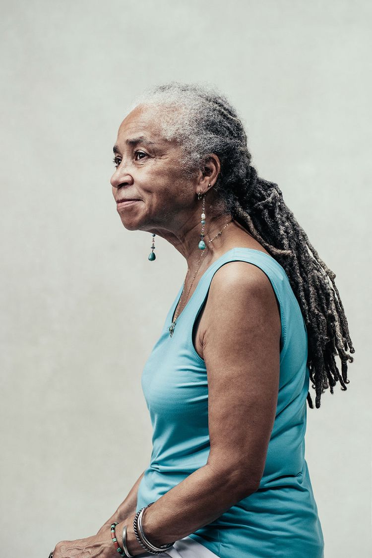 Profile portrait of an elderly Black woman with long dreadlocks wearing a blue tank top and turquoise earrings