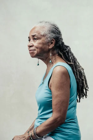 Profile portrait of an elderly Black woman with long dreadlocks wearing a blue tank top and turquoise earrings