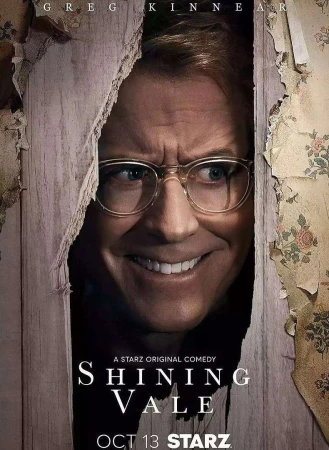 Close-up of Greg Kinnear's face in Shining Vale movie poster, peeking through cracked wood. He wears glasses and smiles.
