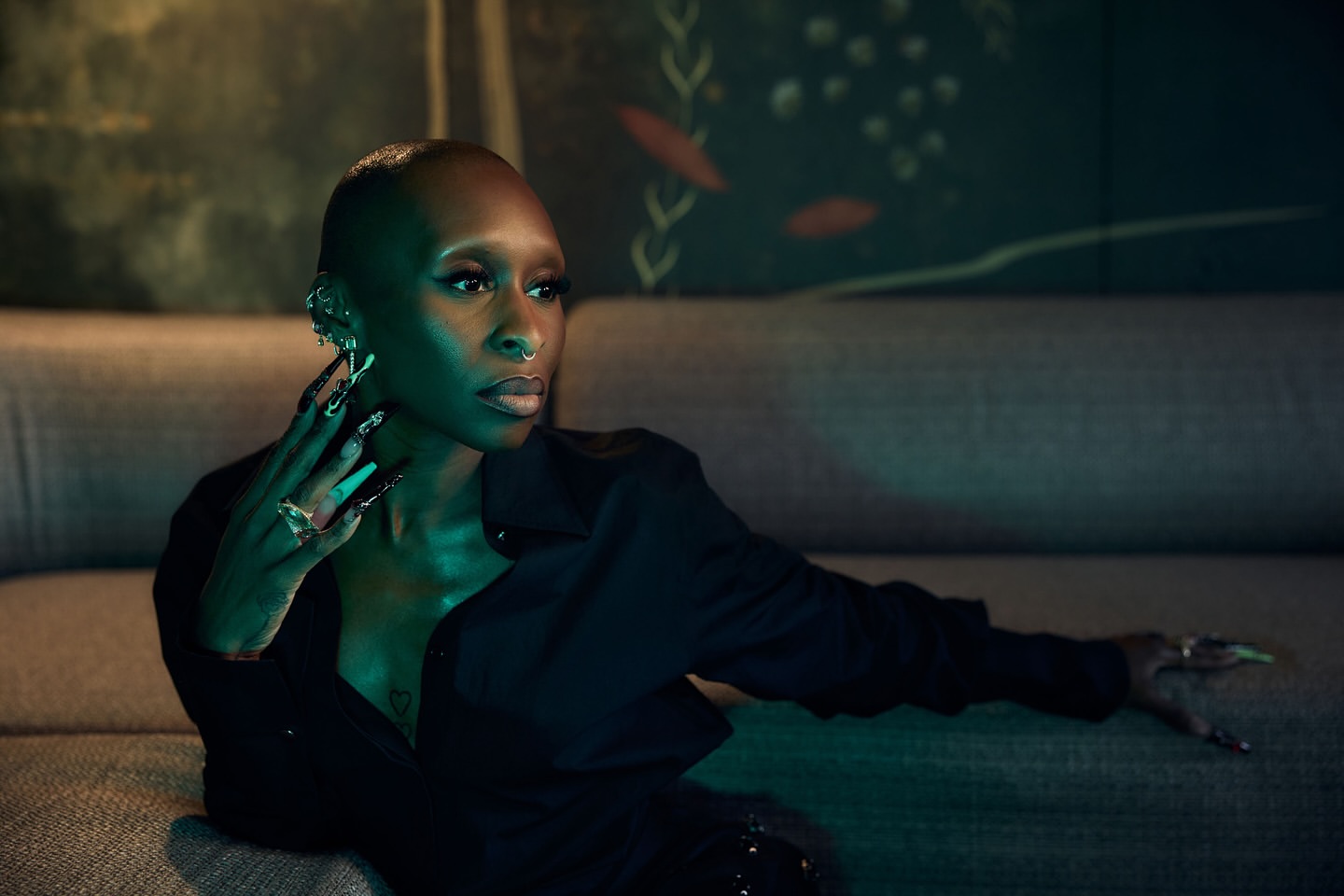 Indoor portrait of a woman with short hair, wearing a black button-down shirt, and sitting on a couch, under blue and green lighting.
