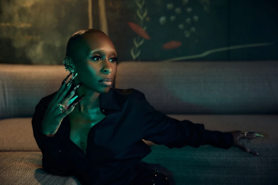 Indoor portrait of a woman with short hair, wearing a black button-down shirt, and sitting on a couch, under blue and green lighting.