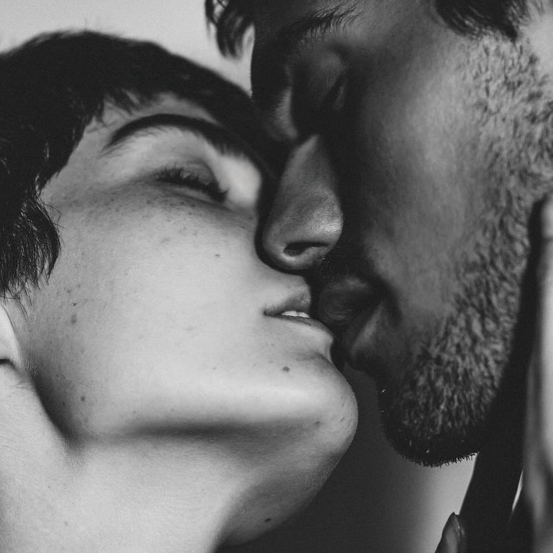 A grayscale image captures a couple kissing, their faces close, showcasing intricate details and textures in a tender moment.