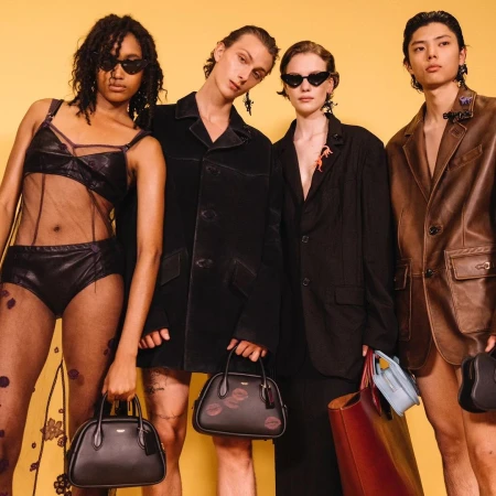 Four fashion models strike a pose in a studio wearing stylish clothing and accessories, showcasing a blend of modern and edgy aesthetics.