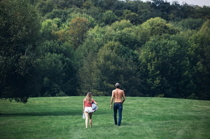 Man and woman walking away across a green field towards a dense forest edge shot by Victoria Will