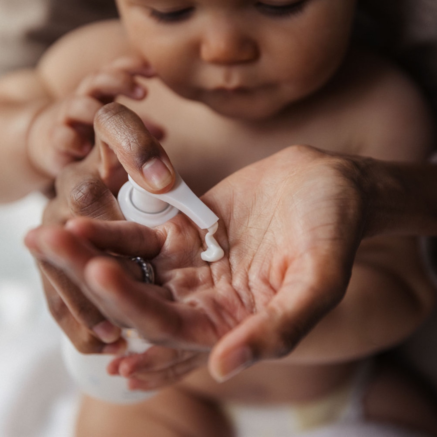 Adult applying lotion to a baby's hand in an indoor setting, featuring a close-up shot with a focus on skincare and baby care.
