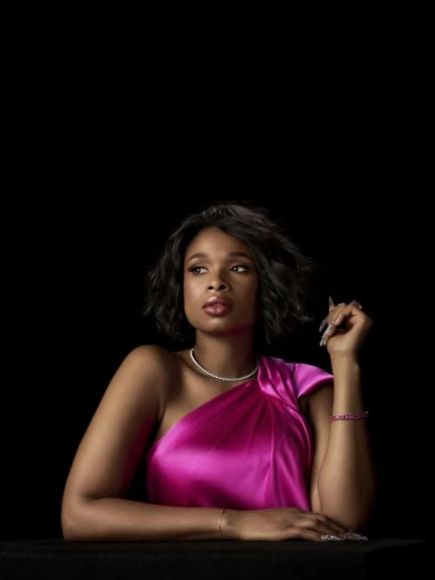 A glamorous portrait of a Black female celebrity with short black hair, wearing a fuchsia gown and diamond jewelry, against a black background.