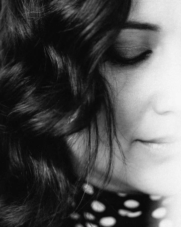 Close-up black and white portrait of a woman with dark wavy hair and closed eyes wearing a polka dot top.