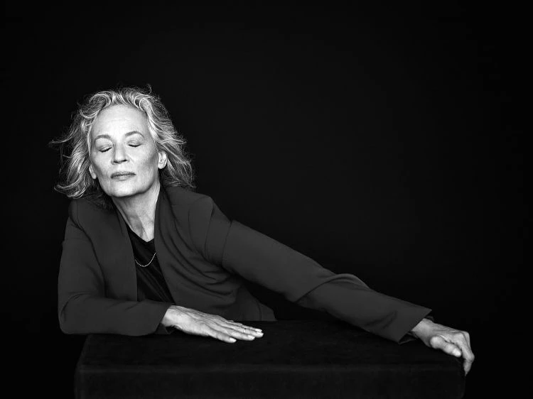 Portrait of Victoria Will in a dark photo studio, wearing a black top, with soft lighting highlighting her face and shoulders.