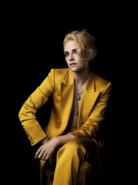 Adult female model poses in a photo studio, wearing a black blazer and sunglasses, with soft studio lighting on a grey backdrop.