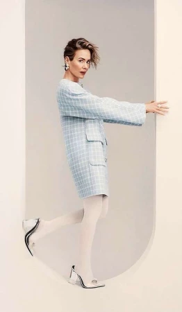 Portrait of actress Sarah Paulson wearing a light blue plaid coat and white tights posing inside an arched doorway.