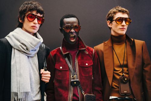 Three models wearing sunglasses and fashionable attire pose indoors. The models are wearing jackets and carrying phone accessories.
