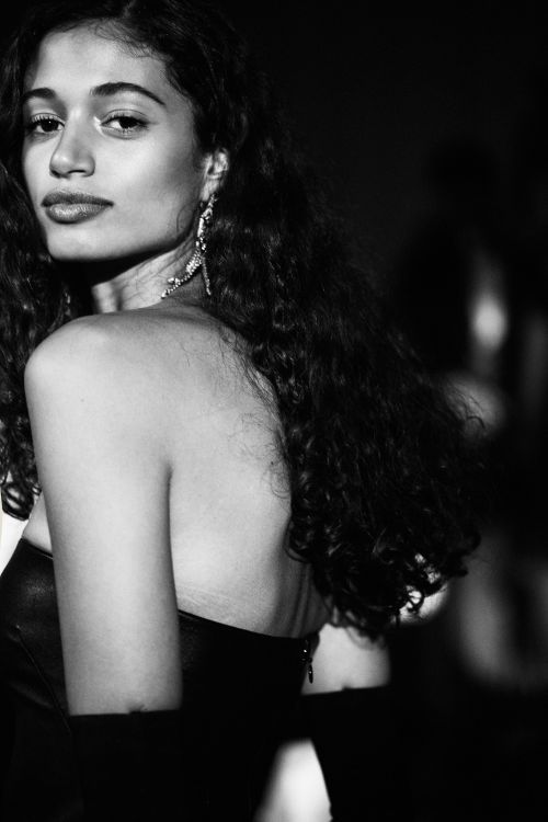 Portrait of a woman with long dark curly hair looking back over her shoulder in a black strapless dress and statement earrings.