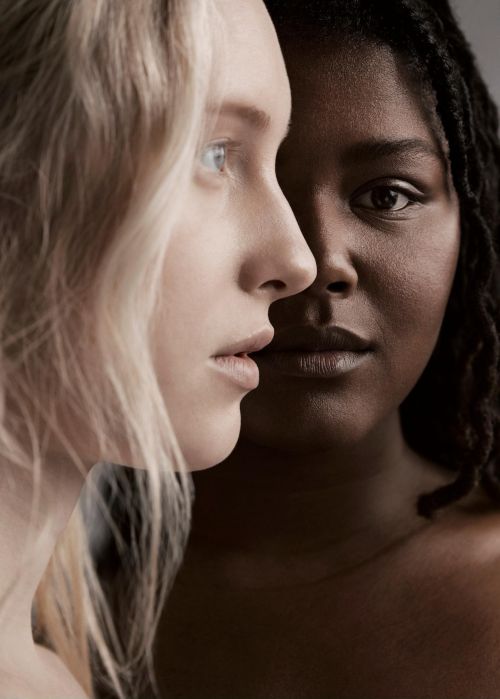 Close-up studio portrait of two women with different skin tones and complementary features in muted lighting, showcasing diverse beauty.