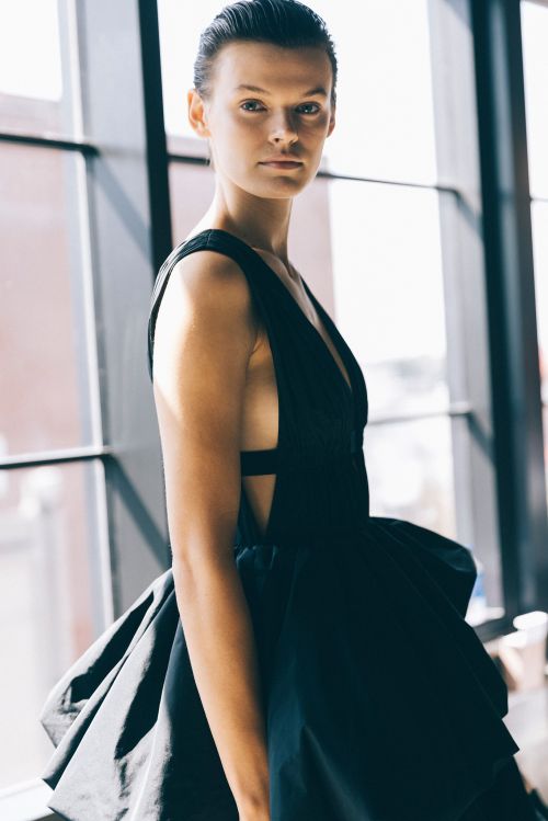 Model in a black v-neck dress posing near a large window by Victoria Will