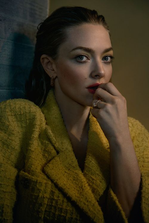 Close-up portrait of Amanda Seyfried wearing a yellow textured blazer, gazing into the camera in a studio-lit, moody setting.