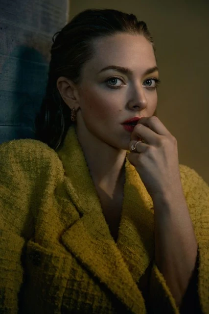 Close-up portrait of Amanda Seyfried wearing a yellow textured blazer, gazing into the camera in a studio-lit, moody setting.
