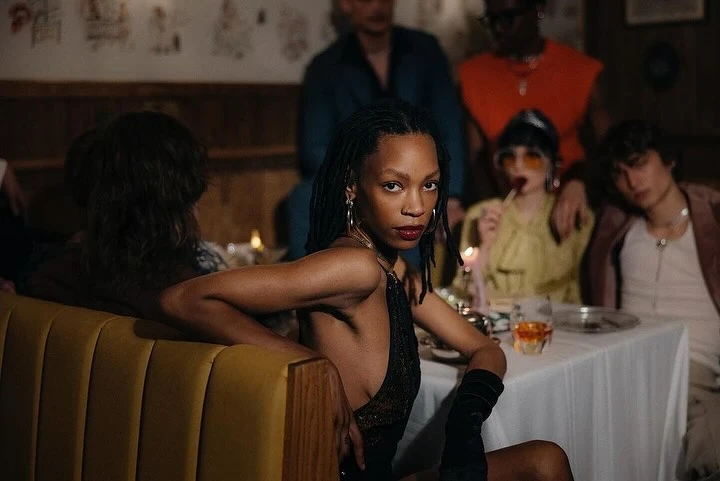 Group of stylish people gathered at a table in a restaurant, dining and socializing. Woman in the foreground faces camera.