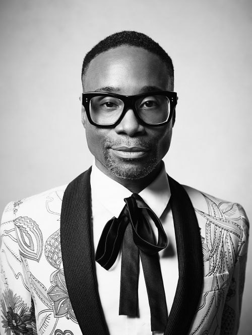Black and white portrait of a person wearing glasses and a patterned suit with a velvet bow tie against a neutral backdrop.