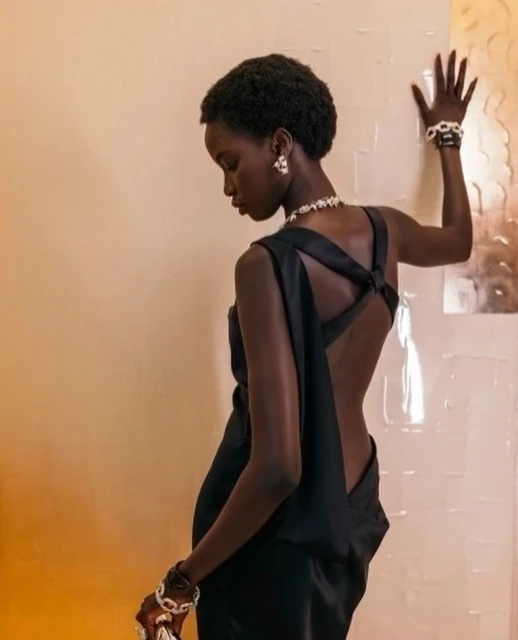 Elegant portrait of a Black woman in a backless black dress, showcasing luxury jewelry in a studio setting with diffused lighting.