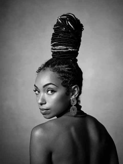 Striking black and white portrait of a stylish African-American woman with locs in a high bun looking over her shoulder.