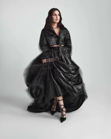 Woman in black crop top and voluminous black skirt posing against a white studio background with motion blur effect.