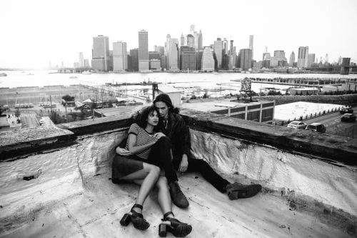 Couple sitting closely on a rooftop corner with a city skyline visible across the water in the background.