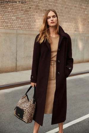 Model in long dark burgundy coat holding a leopard print handbag against a brick building exterior