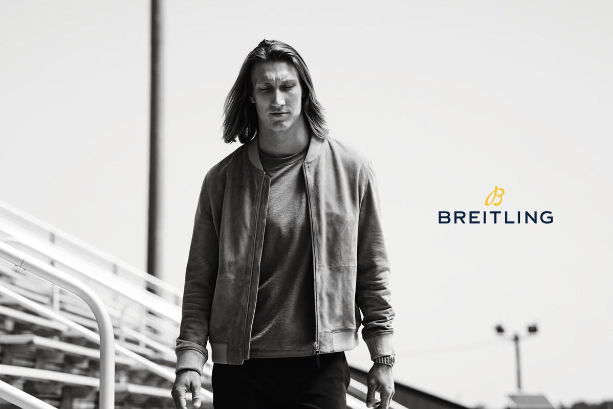 Adult male with long hair in bomber jacket walks on bleachers in a black and white portrait for Breitling watch advertisement.