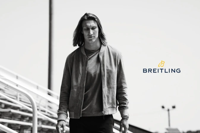Adult male with long hair in bomber jacket walks on bleachers in a black and white portrait for Breitling watch advertisement.