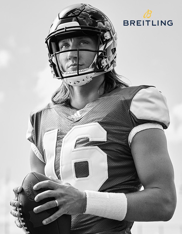 Black-and-white portrait of a football player wearing a helmet and jersey, holding a football, with the Breitling logo at the top right.