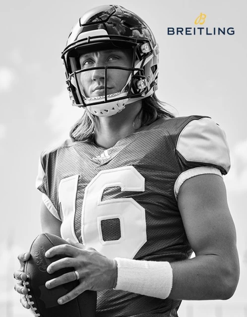 Black-and-white portrait of a football player wearing a helmet and jersey, holding a football, with the Breitling logo at the top right.