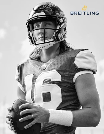 Black-and-white portrait of a football player wearing a helmet and jersey, holding a football, with the Breitling logo at the top right.