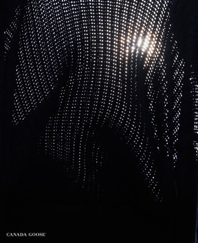 Abstract textured view of black fabric with small perforations and bright sunlight shining through holes creating a starburst effect.