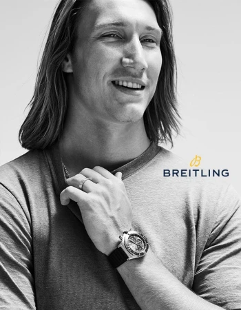 Close up of a handsome adult male model with long hair wearing a silver wristwatch in a black and white advertisement for Breitling.