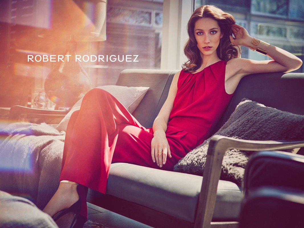 Fashion model in red outfit poses on a couch in a modern apartment with city views. Lifestyle fashion photography for Visie.