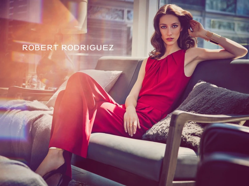 Fashion model in red outfit poses on a couch in a modern apartment with city views. Lifestyle fashion photography for Visie.