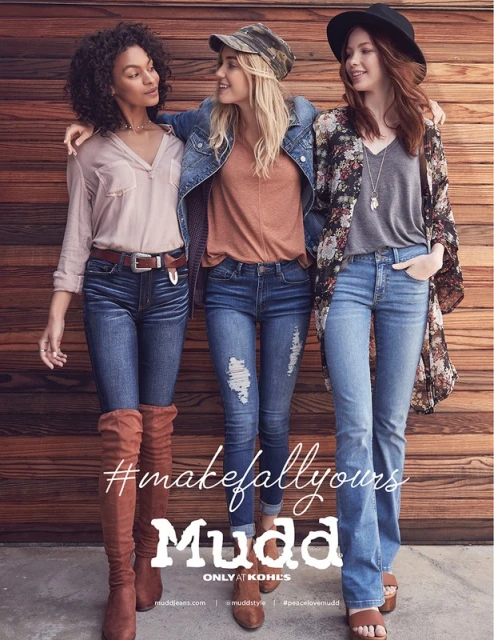 Three women in fashionable casual clothing posing against a wood wall. The women are wearing denim jeans and modern tops. 