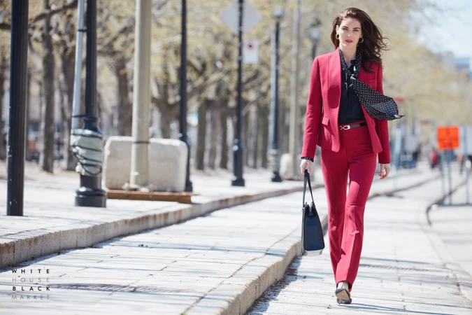 Woman in red pantsuit walking on a city sidewalk holding a black handbag styled by Soraya Dayani