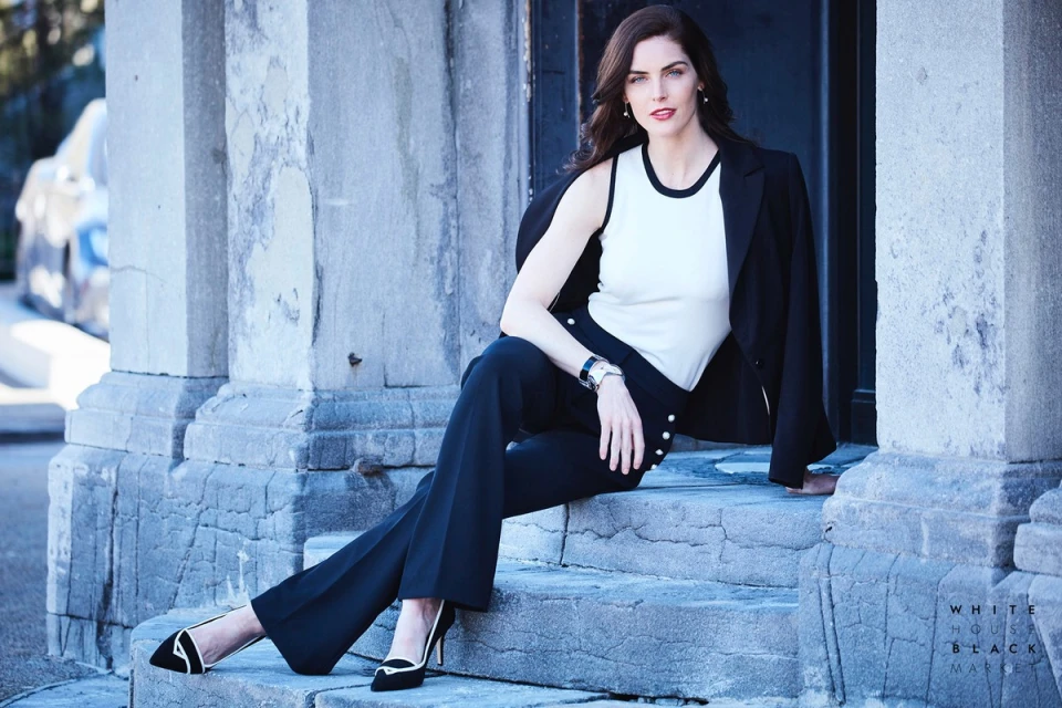 Elegant woman in a black blazer and wide-leg pants sits on stone steps, showcasing a sophisticated and fashionable look against an outdoor backdrop.